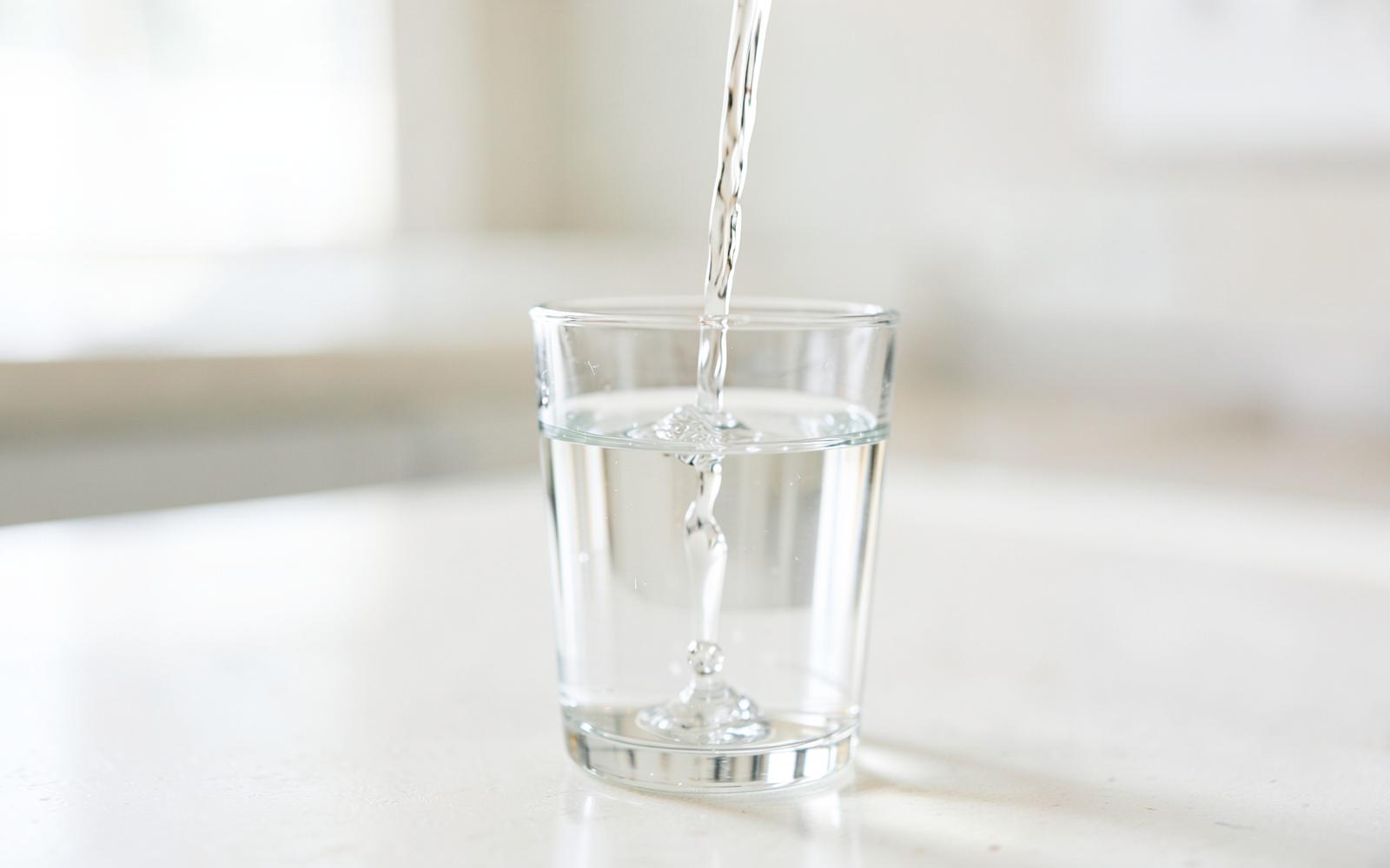 Clear filtered water pouring into a glass on a kitchen counter
